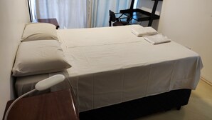 A neatly made bed with white linens, a bedside table with a lamp, and a window with curtains. - APARTAMENTO ACONCHEGANTE LIBERDADE SP (São Paulo)