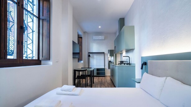 A modern hotel room with a large bed, a small desk, and a kitchenette. - VLC HOST - Reina 168 2 (Valencia)