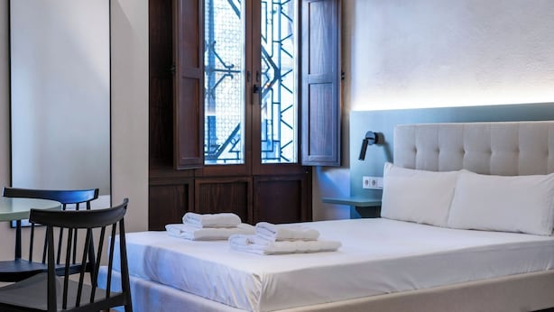 A neatly made bed with white linens, a wooden chair, and a small table with a lamp. - VLC HOST - Reina 168 1 (Valencia)
