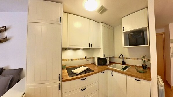 A compact kitchen with white cabinets, a microwave, a sink, and a small countertop.