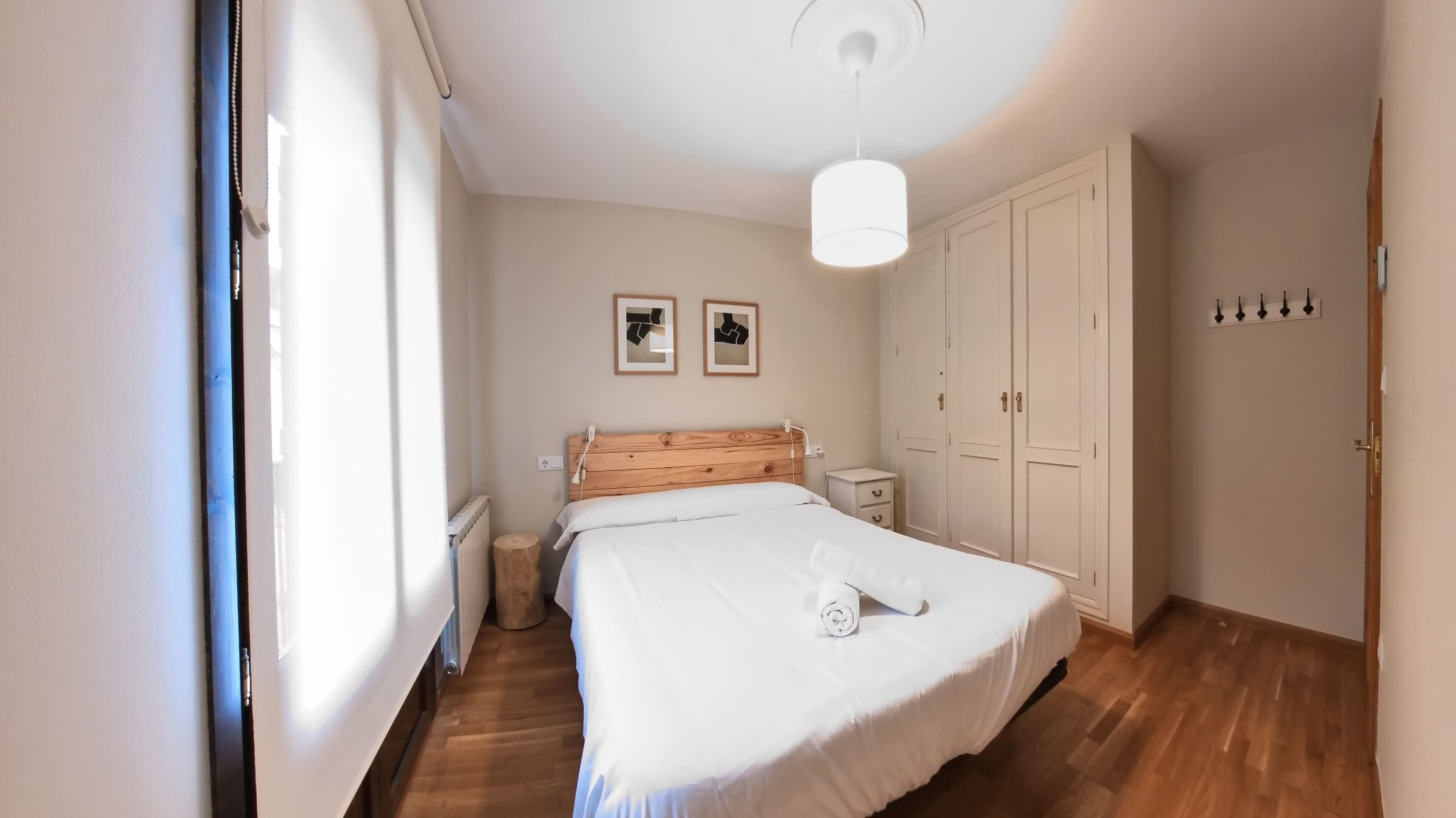 Un dormitorio con cabecera de madera, cama con ropa de cama blanca, mesita de noche, radiador y armario.