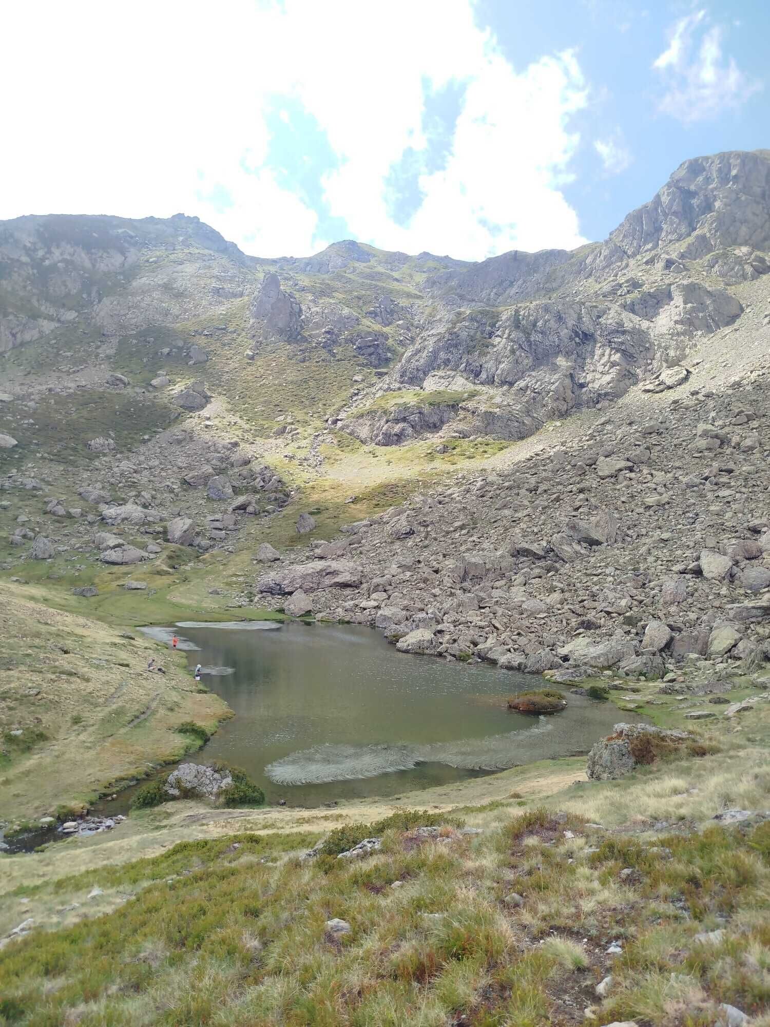 Un paisaje montañoso con un pequeño lago rodeado de terreno rocoso y vegetación escasa.