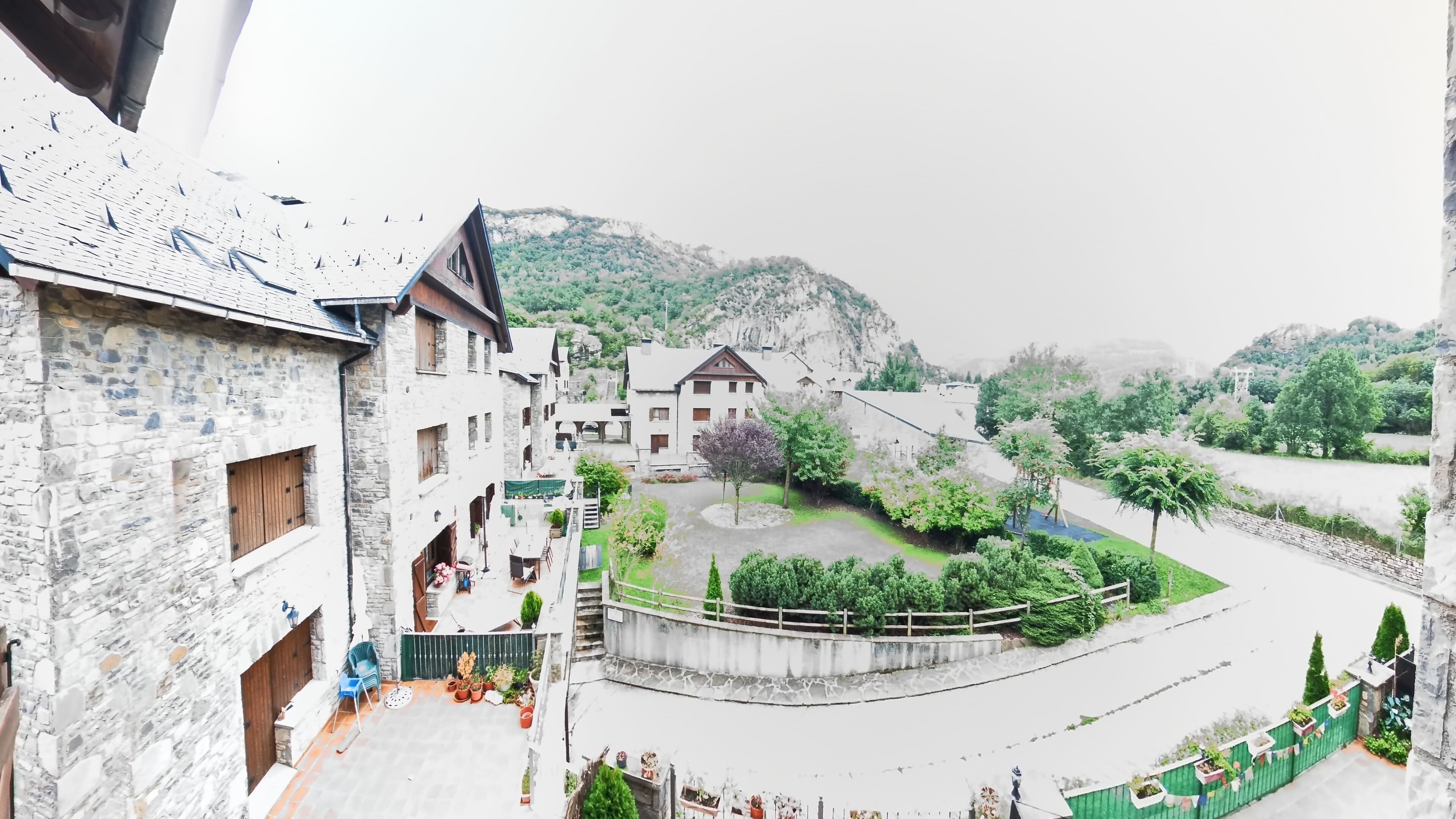 A traditional stone building with multiple balconies, a courtyard with potted plants, and a view of a hilly landscape.