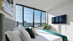 Une chambre moderne dotée d’un grand lit, offrant une vue sur la ville et équipée d’un téléviseur à écran plat.