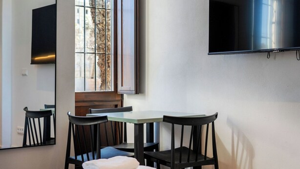 A hotel room with a bed, a small table, two chairs, a TV mounted on the wall, and a window with a view of trees. - VLC HOST - Reina 168 4 (Valencia)