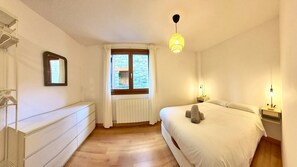 A bedroom with a bed, a dresser, a window with curtains, a radiator, and a hanging light fixture. - Pondiellos 43 - tucasaenlospirineos (Escarrilla)