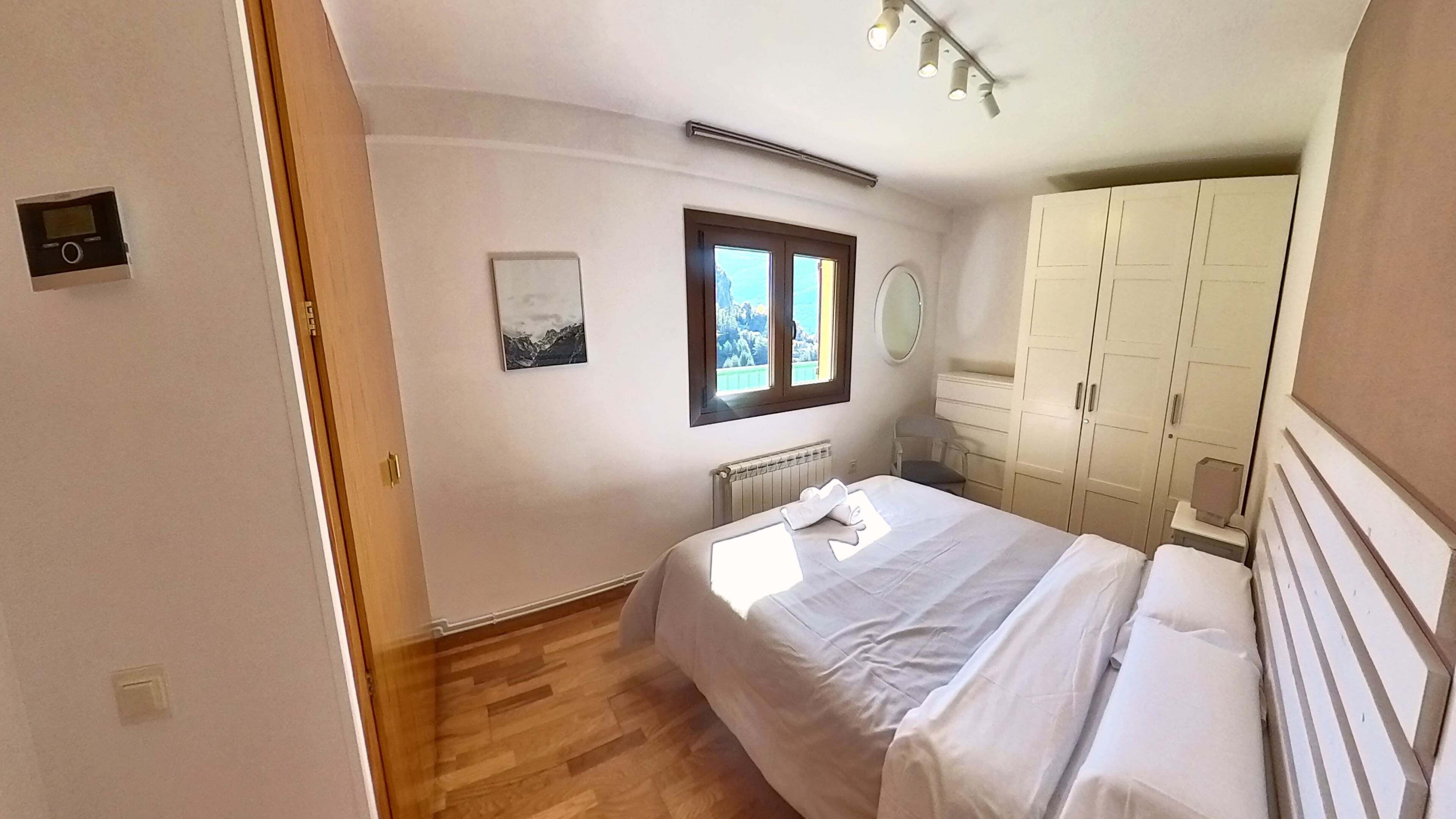 A bedroom with a bed, a window with a view, a radiator, and a wardrobe.