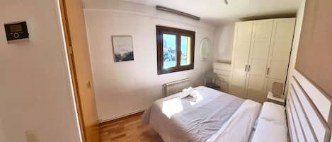A bedroom with a bed, a window with a view, a radiator, and a wardrobe.