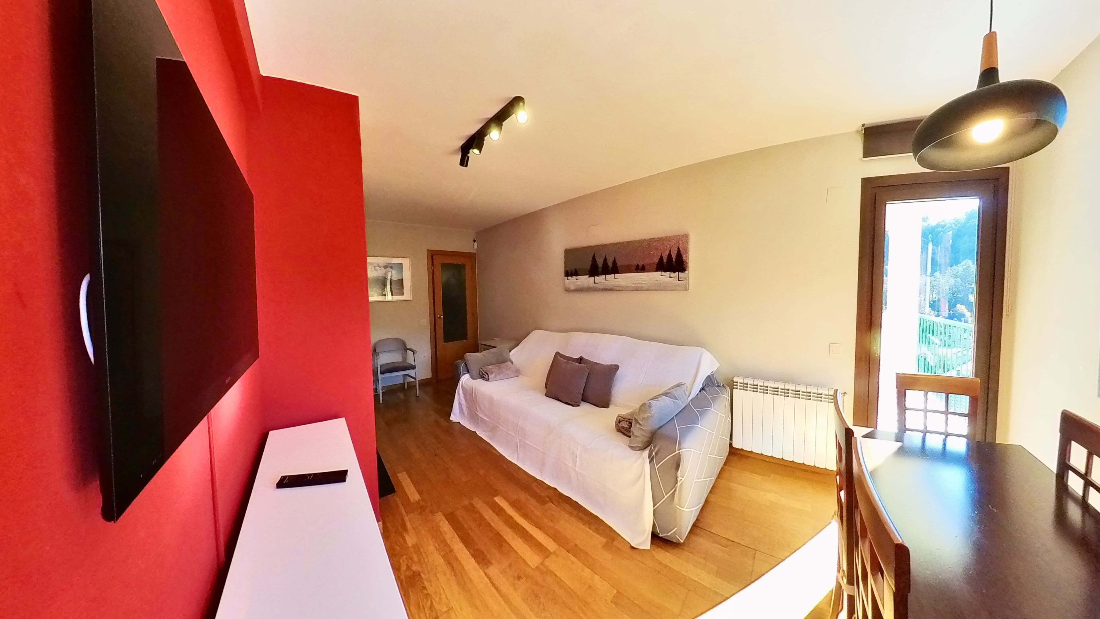 A modern living room with a white sofa, a dining table, a red accent wall, and a painting of trees.