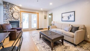 A living room with a stone wall, a fireplace, a sofa, a coffee table, and a dining area with chairs. - Brighton Chalet  (Brighton)