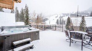 A snow-covered patio with a hot tub, outdoor seating, and a view of a snowy mountain landscape. - Brighton Chalet  (Brighton)