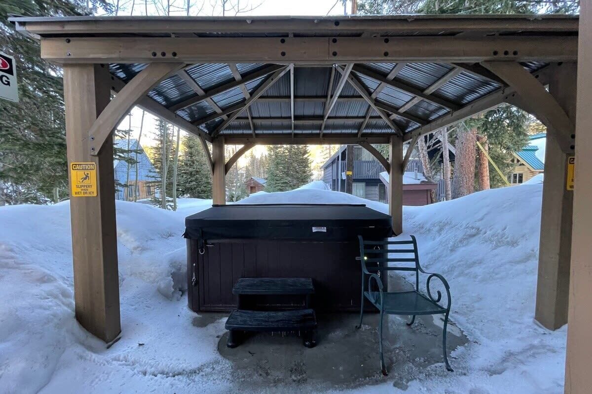 A covered outdoor area with a hot tub, a bench, and a caution sign warning of slippery conditions.