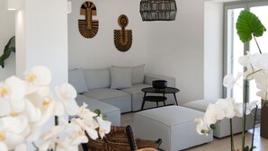 Un salon moderne avec un canapé d’angle, une table basse ronde et un fauteuil en osier.