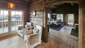 A log cabin interior with a dining area, two white armchairs, a large window, and a hanging light fixture. - Amazing home in Nissedal with WiFi (Nissedal)