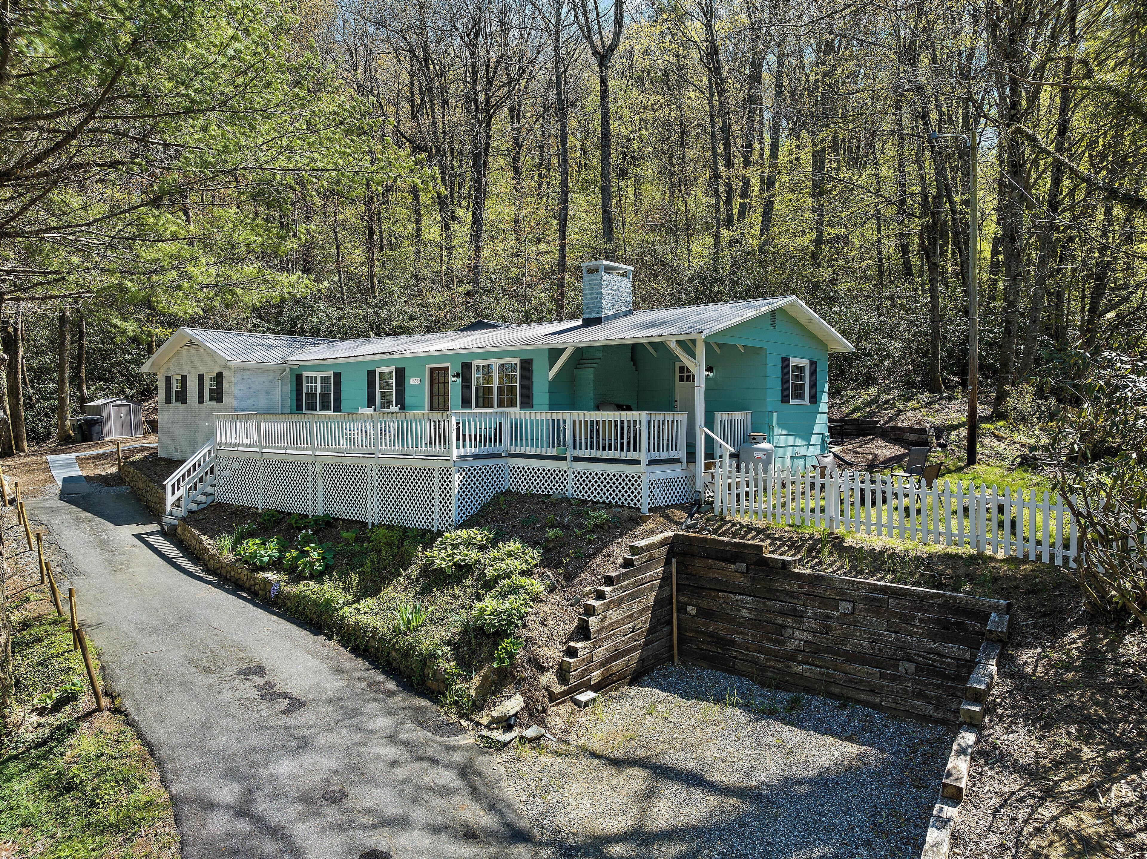 Une cabane turquoise dotée d’un porche, entourée d’une clôture en bois peinte en blanc et d’un mur de soutènement en pierre.