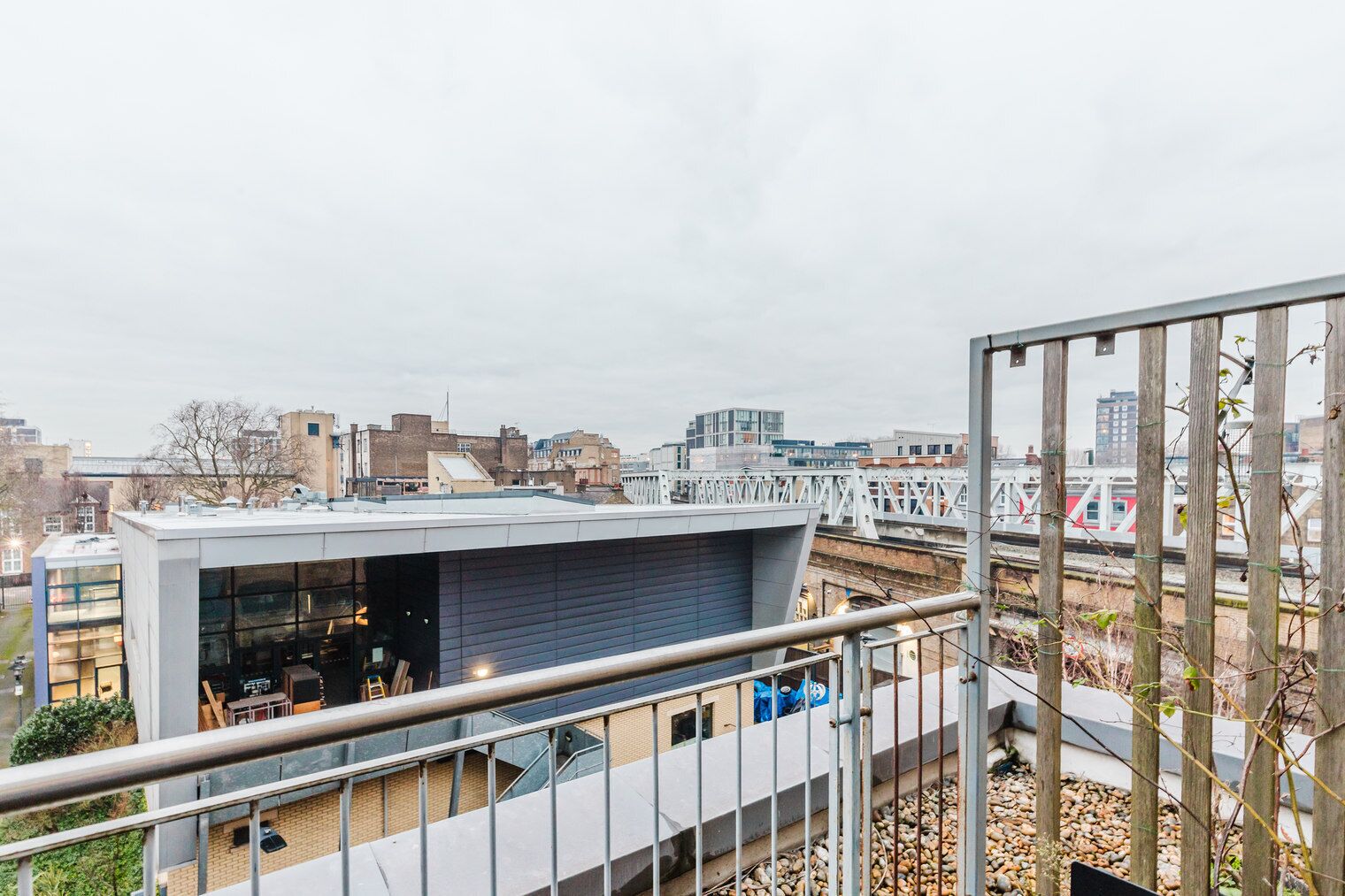 A modern building with a flat roof and large windows, overlooking a cityscape and a railway track.