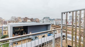 Un bâtiment moderne doté d’un toit plat et de grandes fenêtres, offrant une vue sur le paysage urbain et une voie ferrée.
