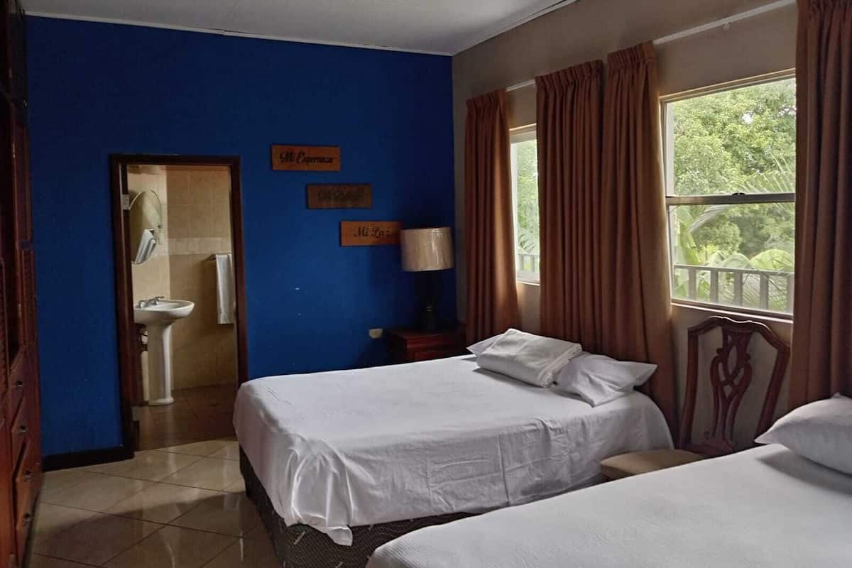 A hotel room with two beds, a bathroom with a sink, and a window with curtains.