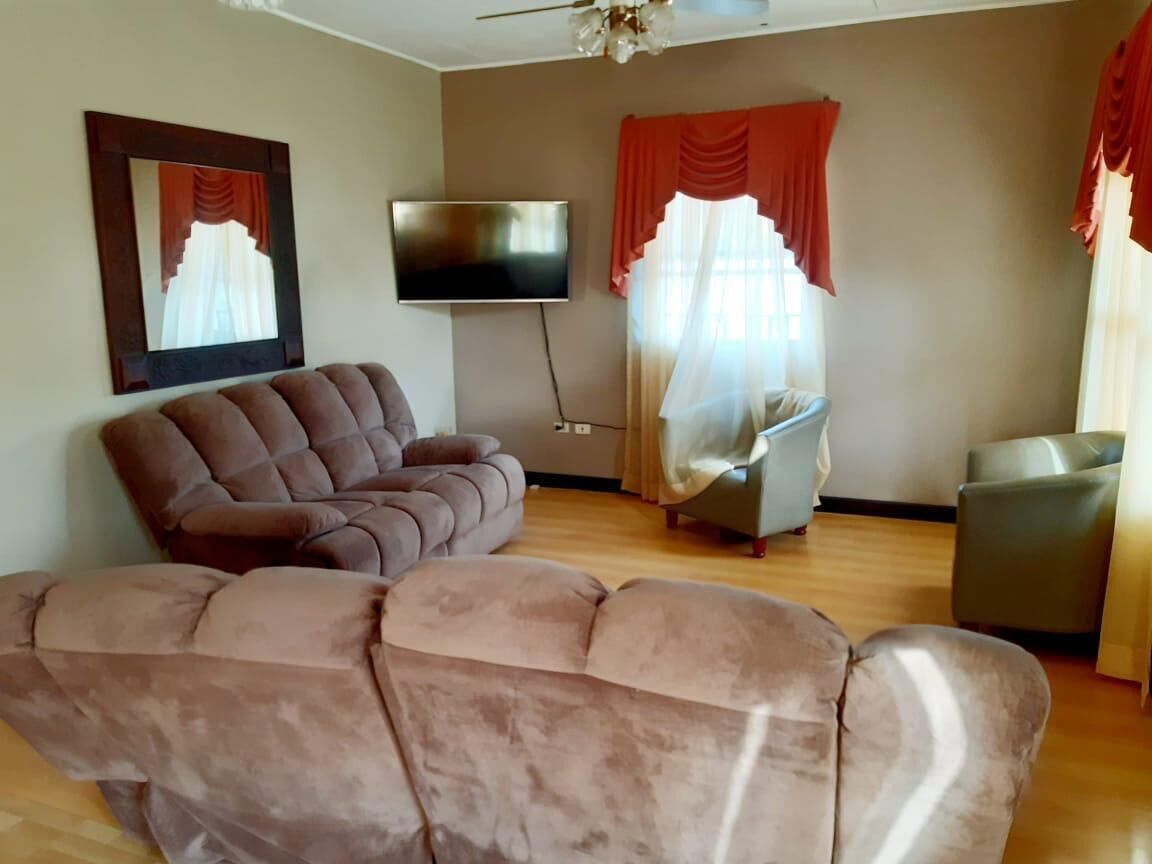 Una sala de estar con un sofá marrón, un sillón gris y un televisor montado en la pared.