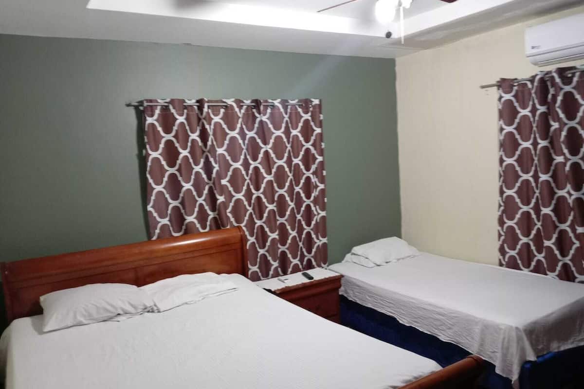 A room with two single beds, a wooden headboard, a nightstand, and patterned curtains.