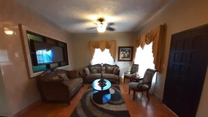 Een woonkamer met een flatscreen televisie, een ronde salontafel, een bank en een fauteuil.