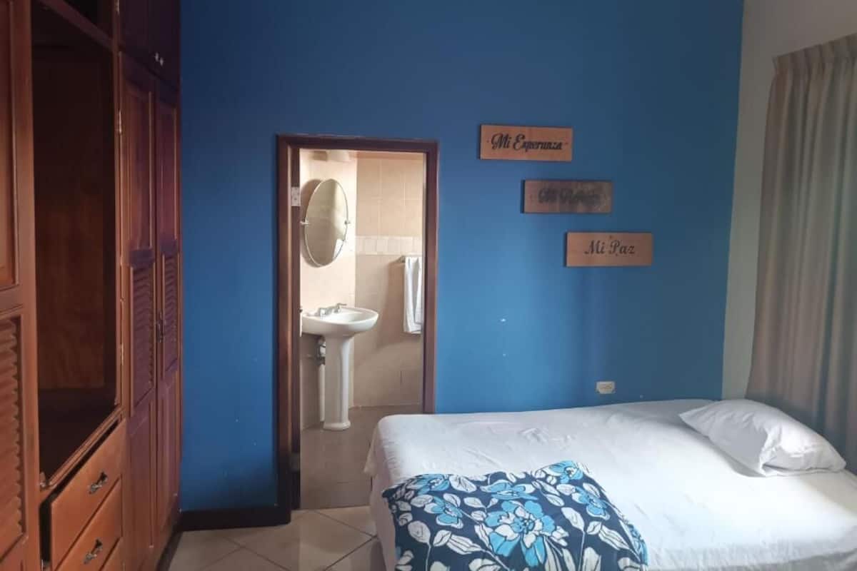 A bedroom with a bed, a wooden wardrobe, a sink, and a door leading to a bathroom.