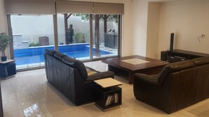 A modern living room with a large glass door leading to a pool area, a sofa, a coffee table, and a TV stand. - Chevron Island Holiday Home (Surfers Paradise)
