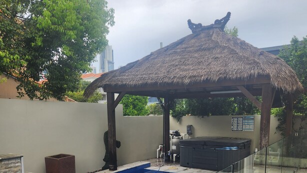 A swimming pool with a glass barrier, a hot tub, and a thatched gazebo. - Chevron Island Holiday Home (Surfers Paradise)