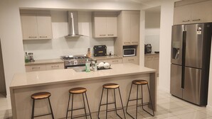 A modern kitchen with a central island, bar stools, a stainless steel refrigerator, a microwave, and a stove. - Chevron Island Holiday Home (Surfers Paradise)