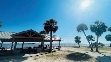 A beachside pavilion with tables and benches, palm trees, and a clear view of the ocean.
