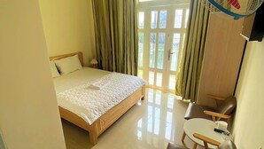 Een hotelkamer met een bed, een tafeltje, een bank, een ventilator en een paar slippers op de vloer.