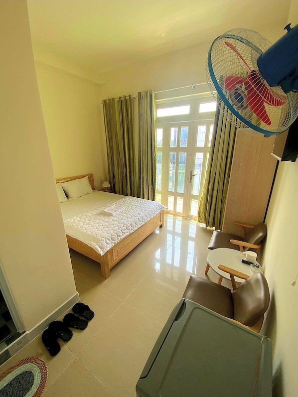 A hotel room with a bed, a small table, a sofa, a fan, and a pair of slippers on the floor. - Anh Thu Hotel (Ho Chi Minh City)