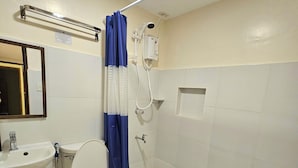 Et badeværelse med toilet, håndvask, bruser og en blå måtte på gulvet.