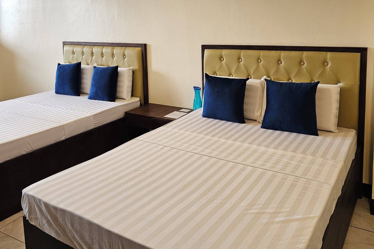 Two single beds with headboards, a small table, and a blue vase.