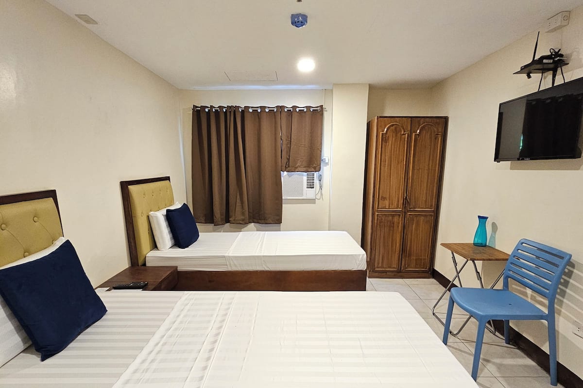 A hotel room with two beds, a wooden wardrobe, a television, and a small table with a chair.