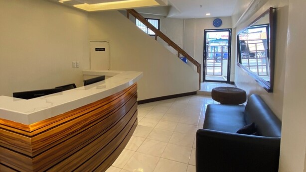 Et moderne reception område med en træreception, en sort sofa, en loftsvifte og en trappe til et udendørs område.
