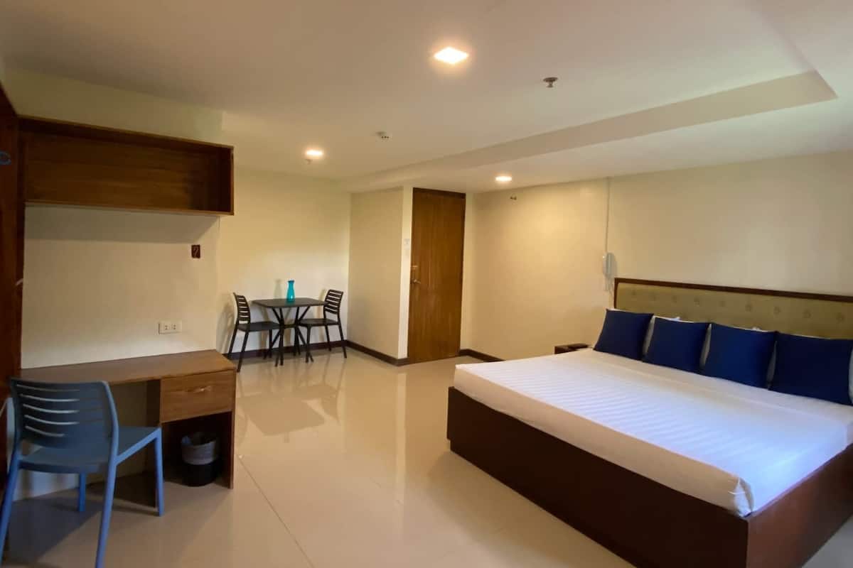 A bedroom with a large bed, a desk, and a chair. There is a small table with chairs in the corner.