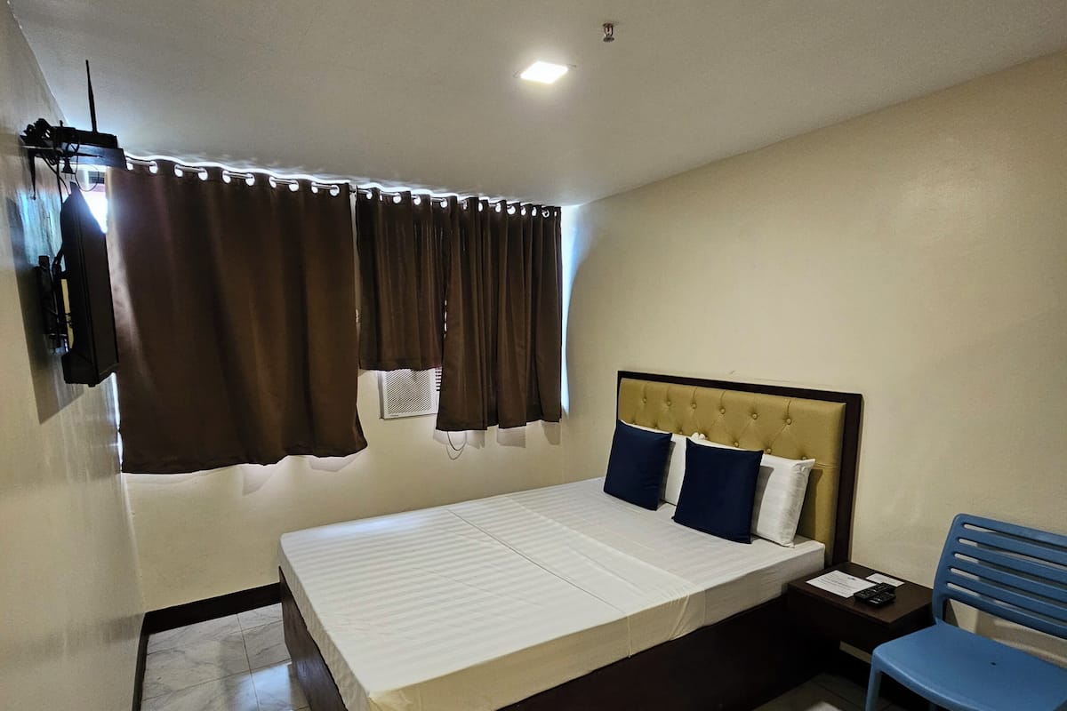 A hotel room with a bed, a nightstand, a chair, and a TV mounted on the wall.