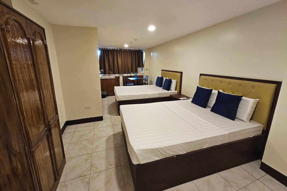 A hotel room with two beds, a wooden wardrobe, a small kitchenette, and a bathroom.