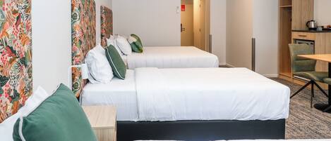 A hotel room with two beds, a desk, a chair, and a kitchenette.