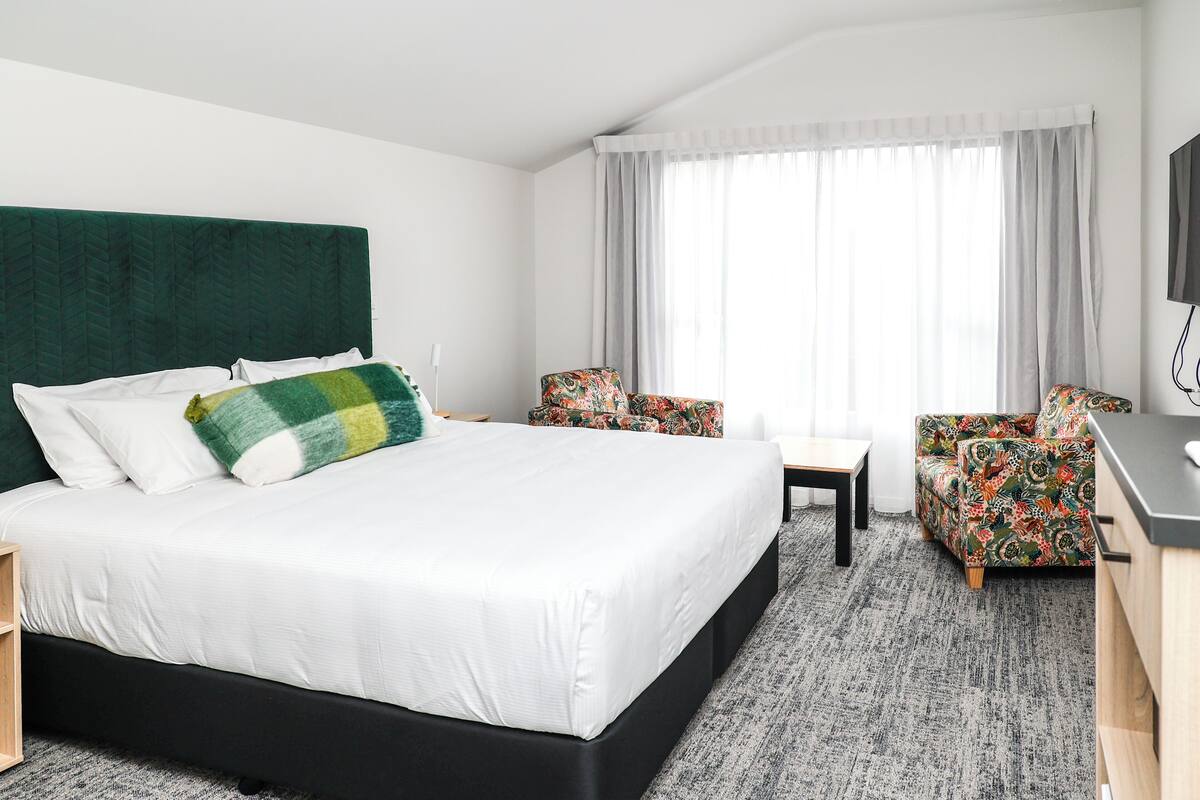 Una habitación de hotel con una cama grande, dos sillones, una mesita y un televisor.