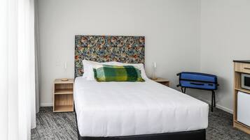 A neatly made bed with a colorful headboard, a bedside table with a lamp, and a blue suitcase on the floor.