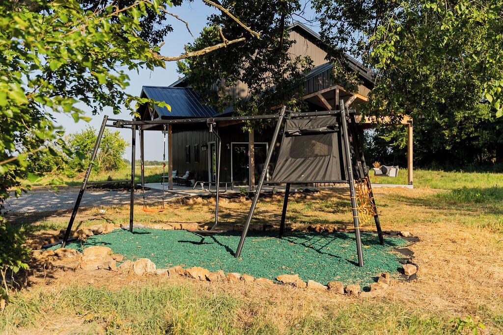 A playground with a swing set and a climbing structure, surrounded by a grassy area and trees.