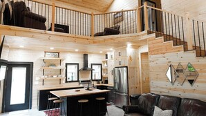 A spacious loft-style living area with a high ceiling, wooden walls, a central kitchen with a large island, a dining area, and a cozy seating area with a leather couch. - Farm Stay in Jasper MO (Jasper)