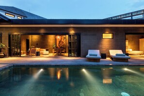 Una casa moderna con piscina, mobiliario exterior e interior bien iluminado.