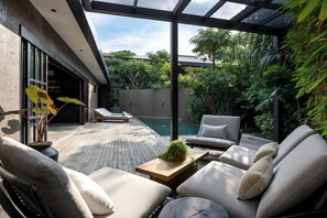 A modern outdoor patio with a pool, lounge chairs, and a wooden table with a plant. - Charming 2-bedroom villa in the center of Pererenan with Private Pool (Bali)