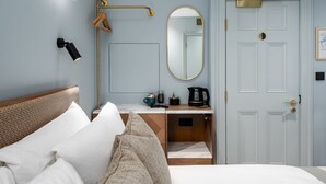 A hotel room with a bed, a bedside table with a coffee maker, a mirror, and a door with a handle. - GuestReady - Fitzroy delight near Regent’s Park (London)