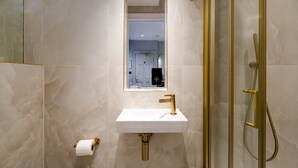 A modern bathroom with a marble floor, a white sink with a gold faucet, and a glass-enclosed shower. - GuestReady - Fitzroy delight near Regent’s Park (London)