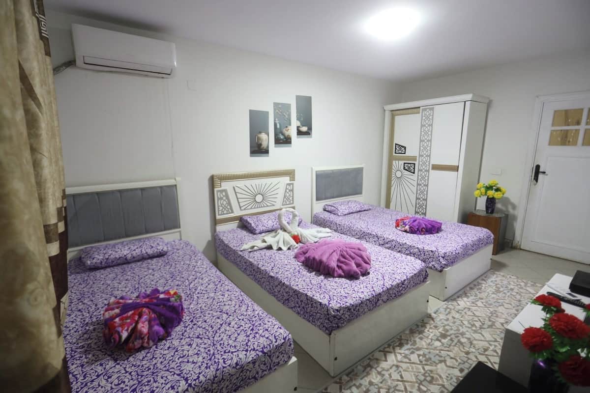 A room with three beds, a wardrobe, and a small table with flowers.