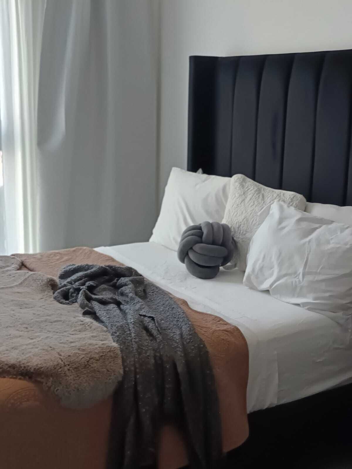A neatly made bed with white linens and a dark headboard, a gray throw blanket, and a dark gray pillow.